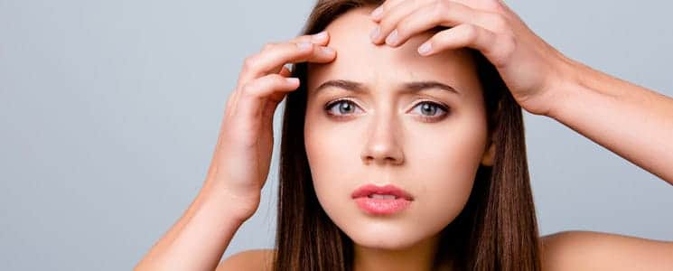 Woman examining acne spot on her forehead