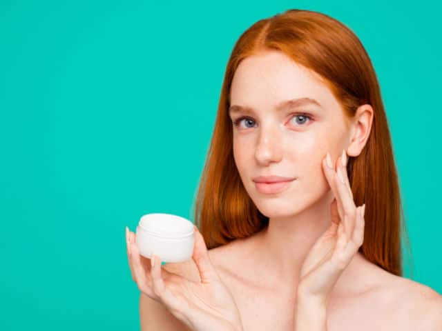 red-haired girl with clean clear face applying cream