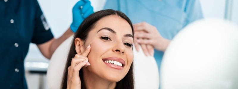 Woman looking in mirror after beauty treatment with hyaluronic acid fillers