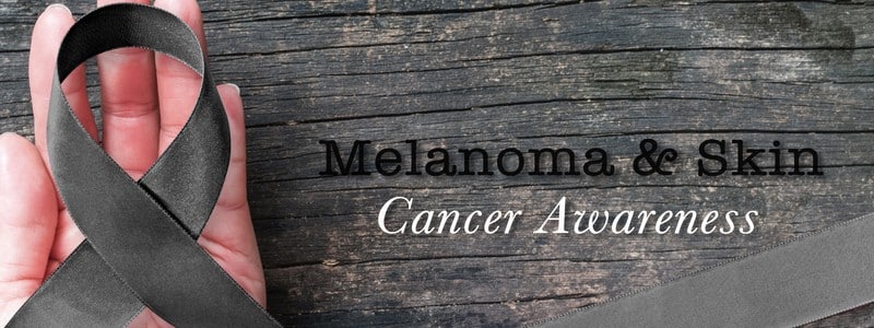 Melanoma and skin cancer black awareness ribbon on human helping hand old aged background
