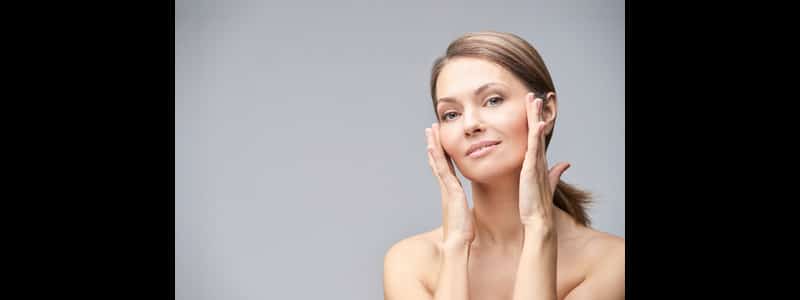 A woman touching her cheeks after getting Radiesse® for facial volume in 2026